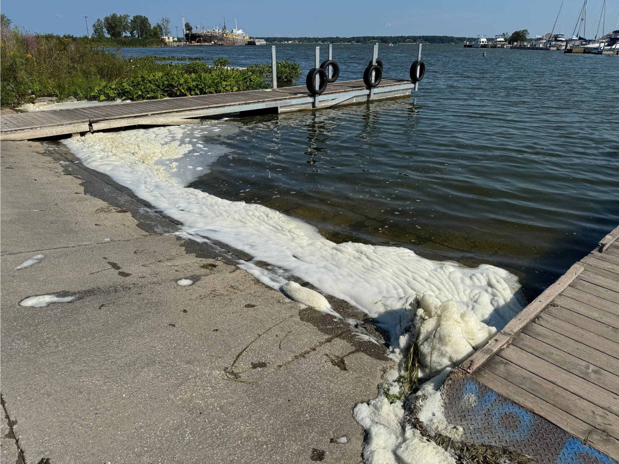 Piles of PFAS foam wash up on the shoreline of a boat launch.